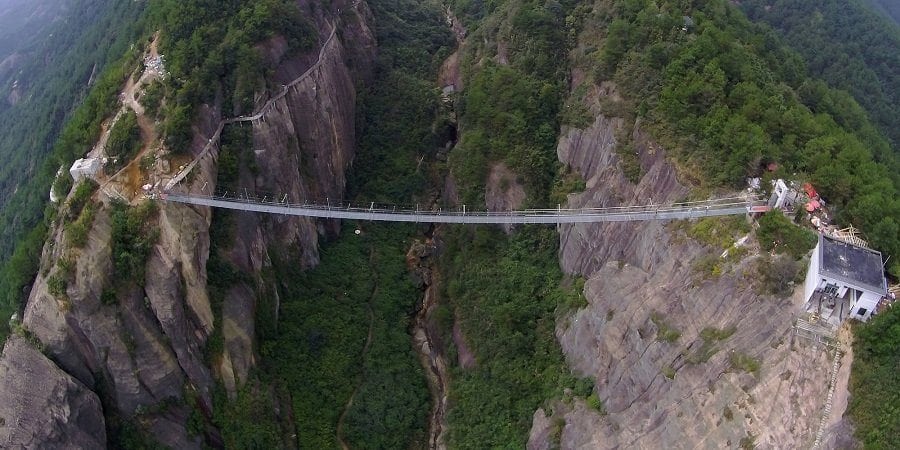 PINGJIANG, CHINA - SEPTEMBER 24:  (CHINA OUT) Tourists walk on a suspension bridge made of glass at the Shiniuzhai National Geological Park on September 24, 2015 in Pingjiang County, China. The 300-meter-long glass suspension bridge, with a maximum height of 180 meters, opened to the public on Thursday.  (Photo by ChinaFotoPress/ChinaFotoPress via Getty Images)