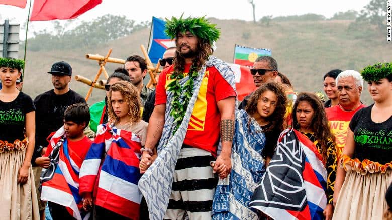 Actor Jason Momoa holds the hands of his children, Nakoa-Wolf Momoa, left, and Lola Momoa, right, as he is welcomed with a hula while visiting elders and Native Hawaiian protesters blocking the construction of a giant telescope on Hawaii's tallest mountain, at Mauna Kea Access Road on Wednesday, July 31, 2019, in Mauna Kea, Hawaii.  (Hollyn Johnson/Hawaii Tribune-Herald via AP)