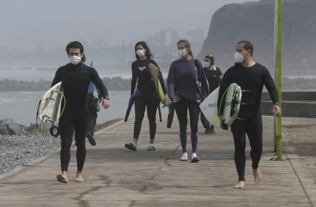 Con mascarillas para protegerse del coronavirus, varios surfistas llegan el jueves 11 de julio de 2020 a la playa reabierta de Waikiki en el distrito de Miraflores, en Lima, Perú. (AP Foto/Martín Mejía)