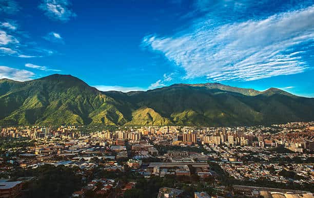 Photograph of Caracas, a Venezuelan city under siege from organized crime and corruption, shot during a beautiful sunny November afternoon displaying the vibrant contrast between the inherent beauty of the city (as shown from a far wide angle shot) and the internal dangers of its daily life.