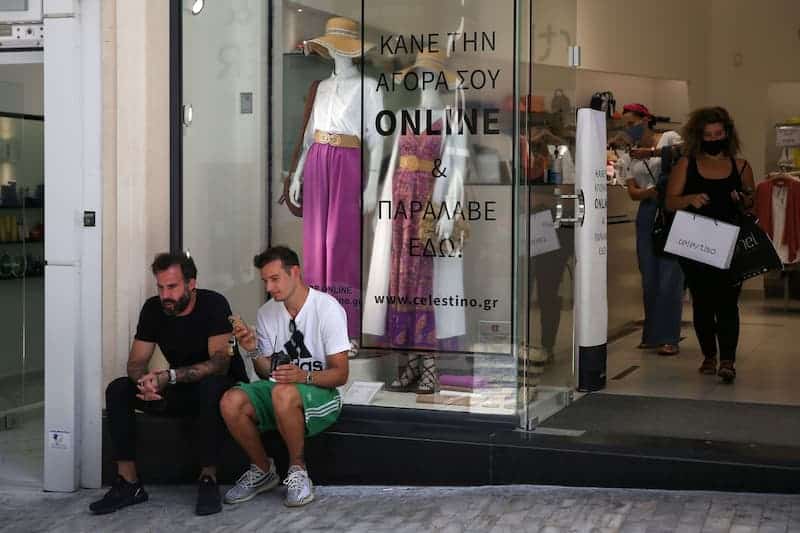 uso de mascarilla Grecia elimina la obligatoriedad del uso de mascarilla en espacios al aire libre Personas afuera de un comercio, sin mascarilla, y una mujer dentro del comercio, con mascarilla, en Grecia