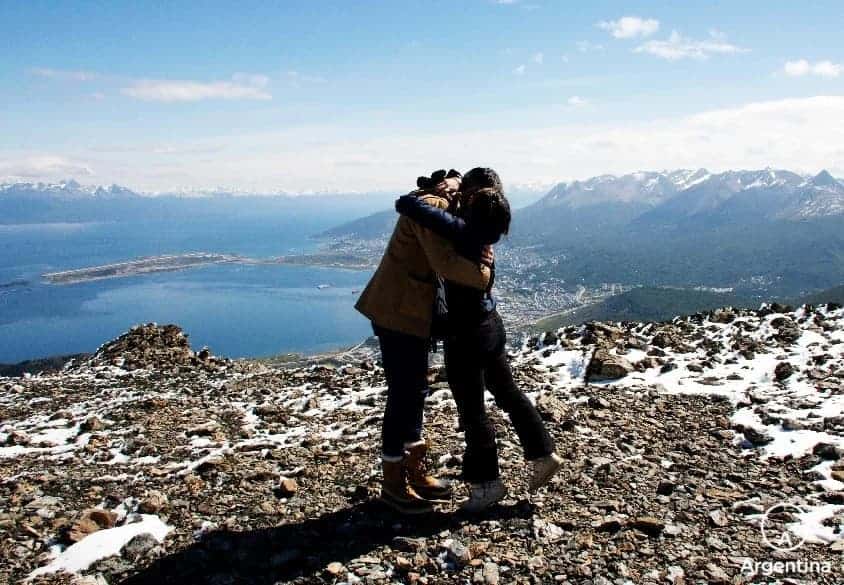 pareja abrazada con ushuaia desde el aire de fondo