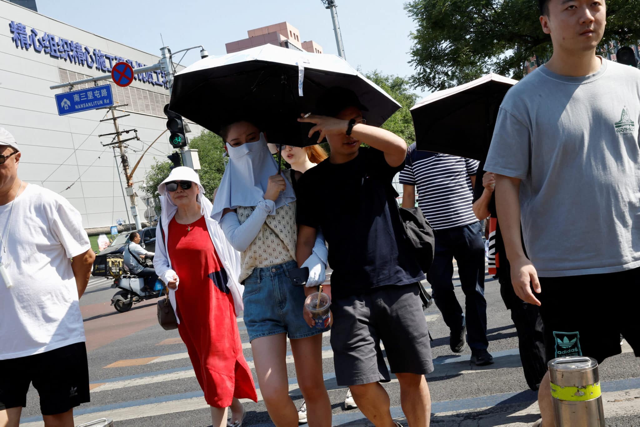 People shield themselves with umbrellas and face masks from the sun amid an orange alert for heatwave in Beijing, China June 22, 2023. REUTERS/Tingshu Wang