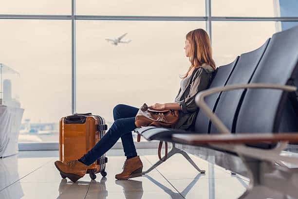 Start of her journey. Beautiful young woman looking out window at flying airplane while waiting boarding on aircraft in airport lounge