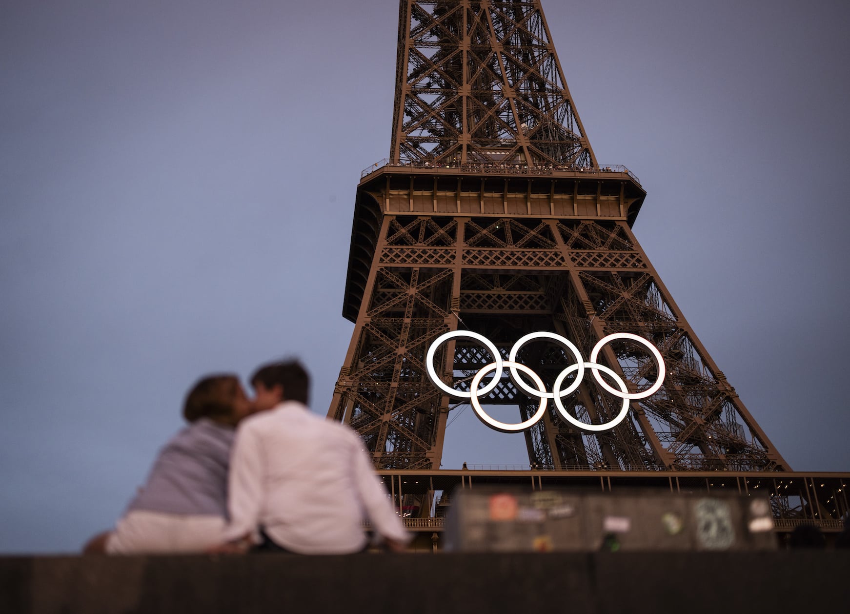 PARIS, FRANCE - JUNE 27: A couple kiss under the Eiffel Tower as the Olympic Rings are displayed during previews ahead of the Paris 2024 Olympic Games on June 27, 2024 in Paris, France. (Photo by Ryan Pierse/Getty Images)