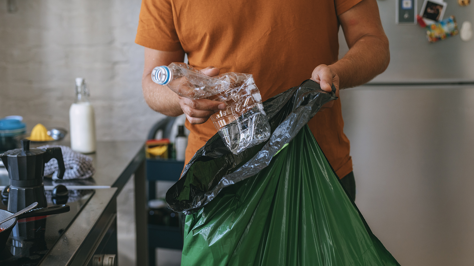 Apuesto joven sosteniendo una bolsa de basura verde y una botella de plástico