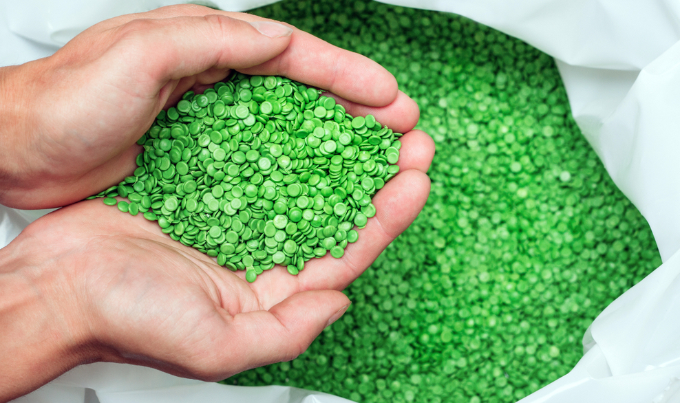 A hands hold or touching biodegradable plastic pellets, plastic polymer dye granules color clear green