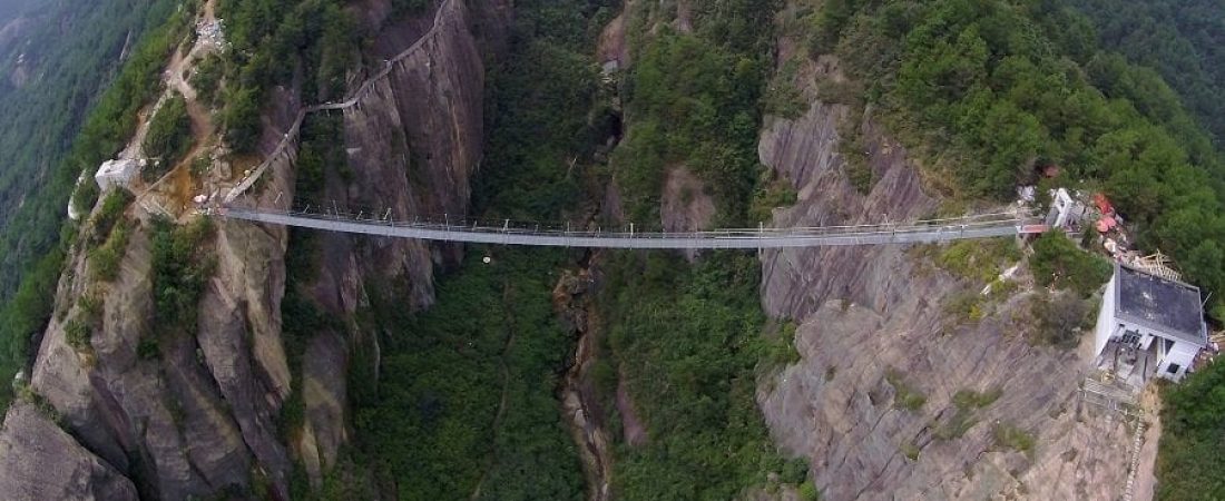 PINGJIANG, CHINA - SEPTEMBER 24:  (CHINA OUT) Tourists walk on a suspension bridge made of glass at the Shiniuzhai National Geological Park on September 24, 2015 in Pingjiang County, China. The 300-meter-long glass suspension bridge, with a maximum height of 180 meters, opened to the public on Thursday.  (Photo by ChinaFotoPress/ChinaFotoPress via Getty Images)