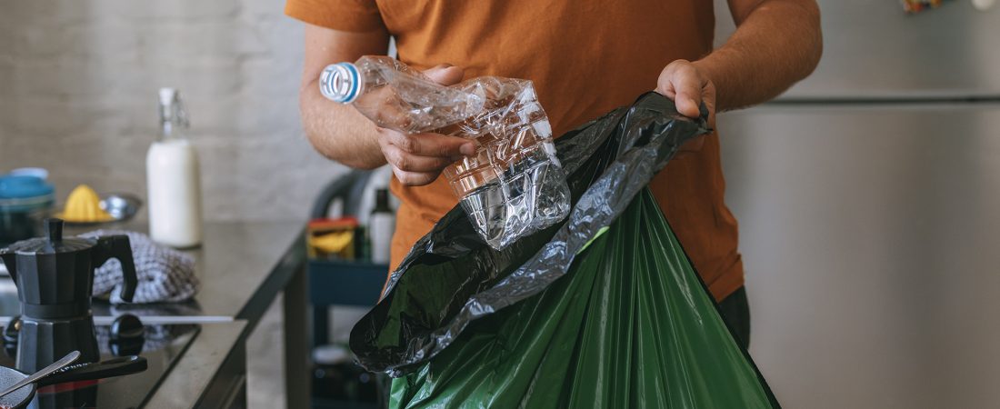 Apuesto joven sosteniendo una bolsa de basura verde y una botella de plástico