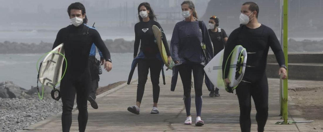 Con mascarillas para protegerse del coronavirus, varios surfistas llegan el jueves 11 de julio de 2020 a la playa reabierta de Waikiki en el distrito de Miraflores, en Lima, Perú. (AP Foto/Martín Mejía)