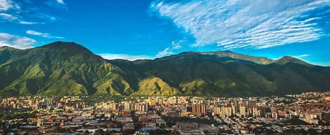 Photograph of Caracas, a Venezuelan city under siege from organized crime and corruption, shot during a beautiful sunny November afternoon displaying the vibrant contrast between the inherent beauty of the city (as shown from a far wide angle shot) and the internal dangers of its daily life.