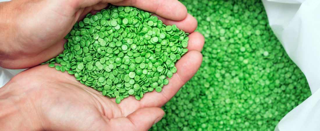 A hands hold or touching biodegradable plastic pellets, plastic polymer dye granules color clear green