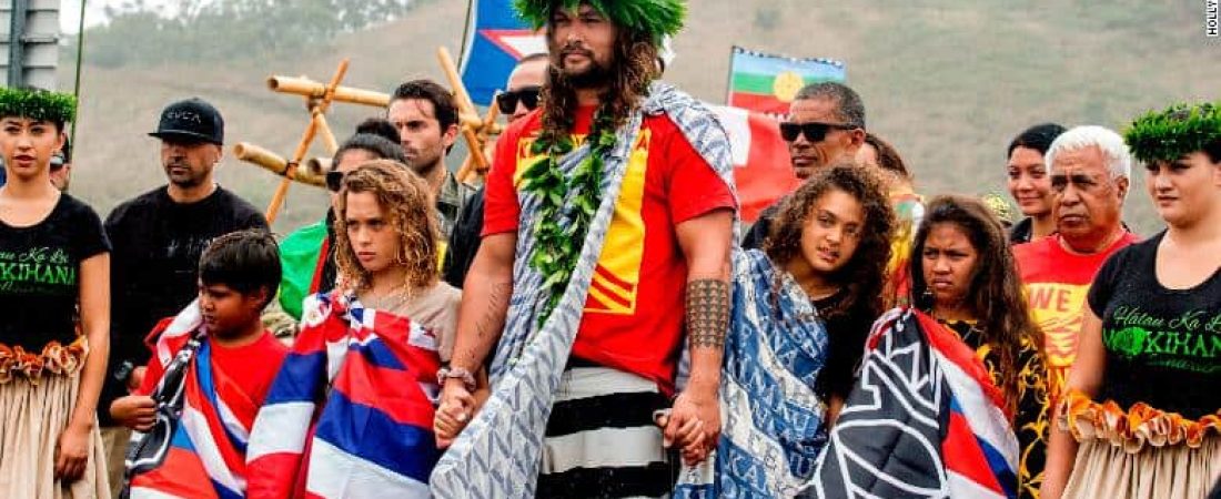 Actor Jason Momoa holds the hands of his children, Nakoa-Wolf Momoa, left, and Lola Momoa, right, as he is welcomed with a hula while visiting elders and Native Hawaiian protesters blocking the construction of a giant telescope on Hawaii's tallest mountain, at Mauna Kea Access Road on Wednesday, July 31, 2019, in Mauna Kea, Hawaii.  (Hollyn Johnson/Hawaii Tribune-Herald via AP)