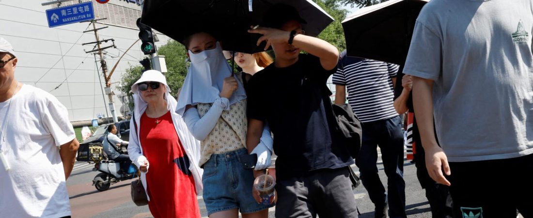 People shield themselves with umbrellas and face masks from the sun amid an orange alert for heatwave in Beijing, China June 22, 2023. REUTERS/Tingshu Wang